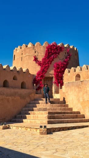 Tourist at an Omani fort with cascading bougainvillea — day trip from Muscat for families