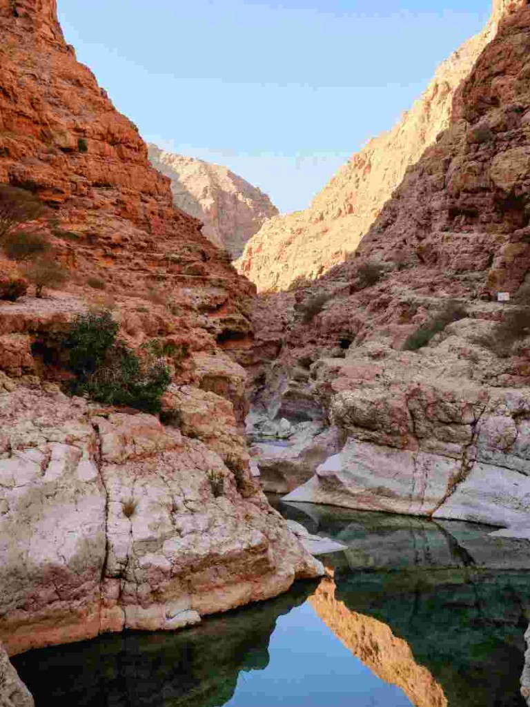 Still pool reflecting red canyon walls at Wadi Shab on a day trip from Muscat