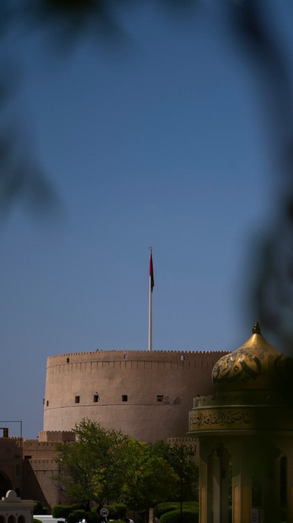 Nizwa Fort with the Omani flag flying above the round tower and a gilded dome in front