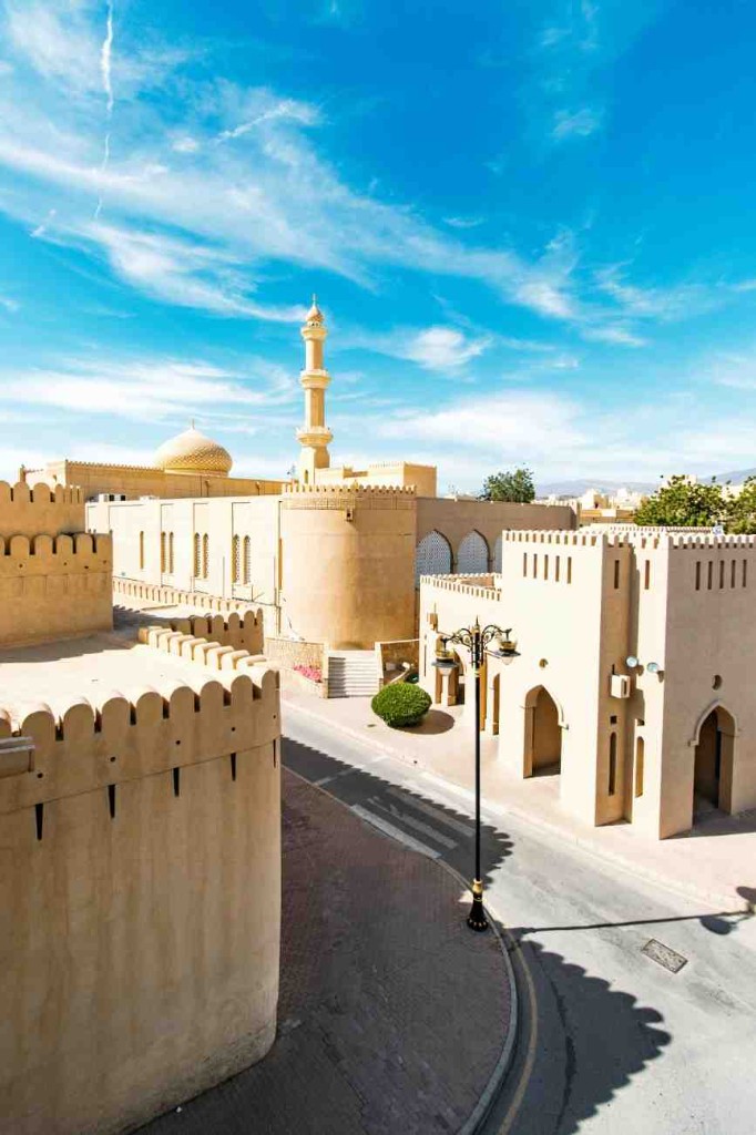 Nizwa old town with crenellated walls, a minaret and a street lamp along the road