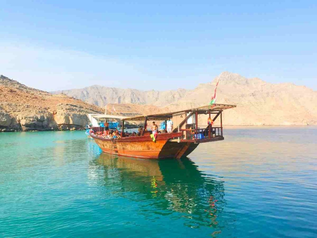 Traditional wooden dhow on turquoise water with rocky Omani mountains behind it