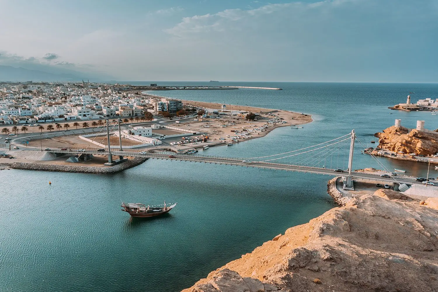 Scenic view of Sur city in Oman featuring traditional dhow boats, coastal architecture, and the iconic lighthouse during a guided city tour